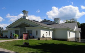 View of the white exterior of the Norman Rockwell museum with blue sky and green grass enhancing the view. 