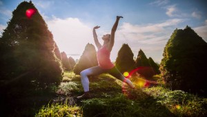 woman reaches to the blue skies above in warrior pose on the lush grounds of Kripalu