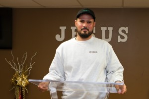 Pastor Thiago Oliveira in his Guido's shirt stands at his chuch's lucite lectern.