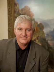 Van Shields, Executive Director of the Berkshire Museum, poses for headshot in front of large landscape oil painting.