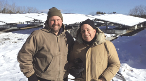 Chris Marsden and Stephen Shatz smile in front of a snow covered solar farm.
