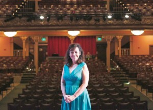 Kate Maguire, CEO of Berkshire Theater Group poses in a blue dress contrasted against the regal interior of Pittsfield's Colonial Theater.