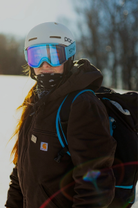 A woman with long brown hair wears snow gear while skiing.