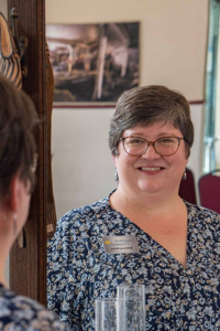 A woman with short brown hair and glasses smiles into a mirror.