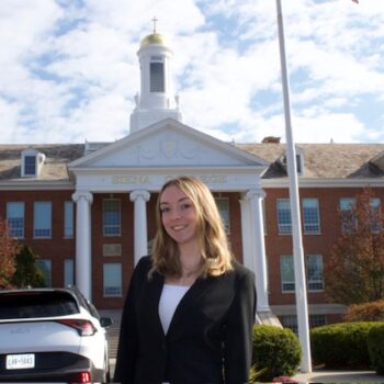 Person smiling at camera standing in front of building